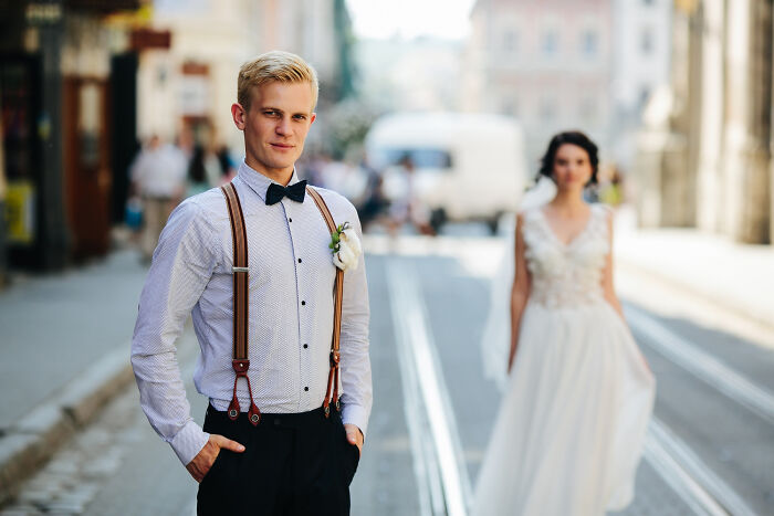 A handsome groom in suspenders and bow tie with a bride in a wedding dress in the background, hinting at unforgettable breakups.