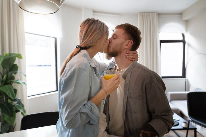 A loving couple shares a kiss, with the woman holding a glass of juice. This image offers a sharp contrast to heartbroken breakups.
