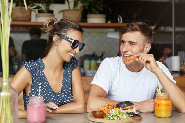 A smiling couple at a cafe, enjoying food and drinks, looking happy. This image contrasts with themes of heartbroken breakups.