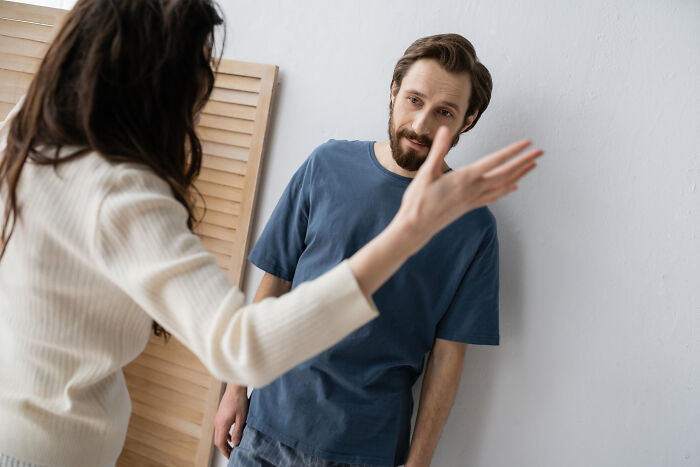 A woman angrily gestures at a man leaning against a wall, symbolizing a painful breakup and heartbroken feelings.