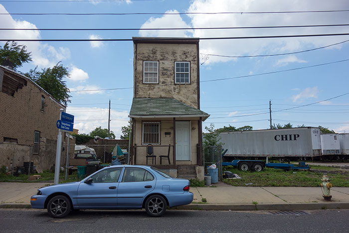 Narrow urban street with a small aging house and parked blue car