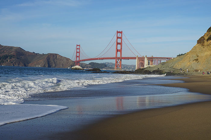 Golden Gate Bridge viewed from a sandy beach with ocean waves