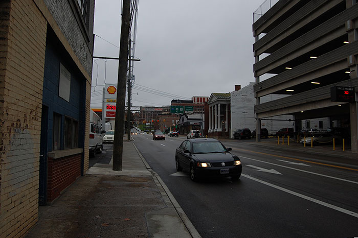 Empty city street with dark cloudy sky and few cars on road