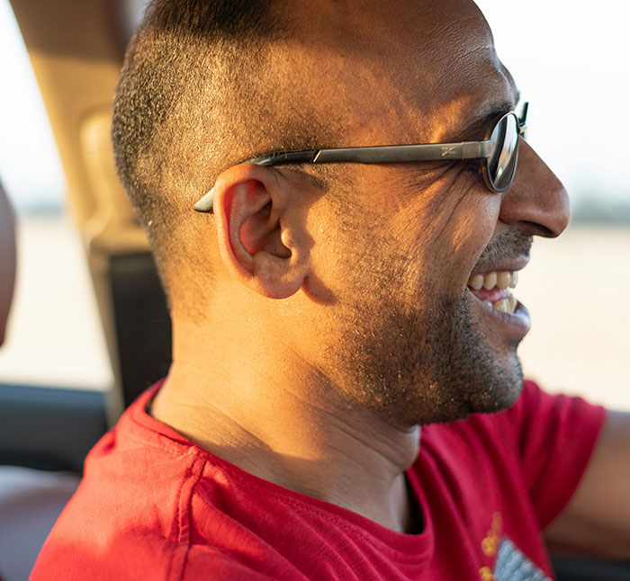 Man in sunglasses and red shirt, smiling while driving. Road rage can impact even happy drivers.