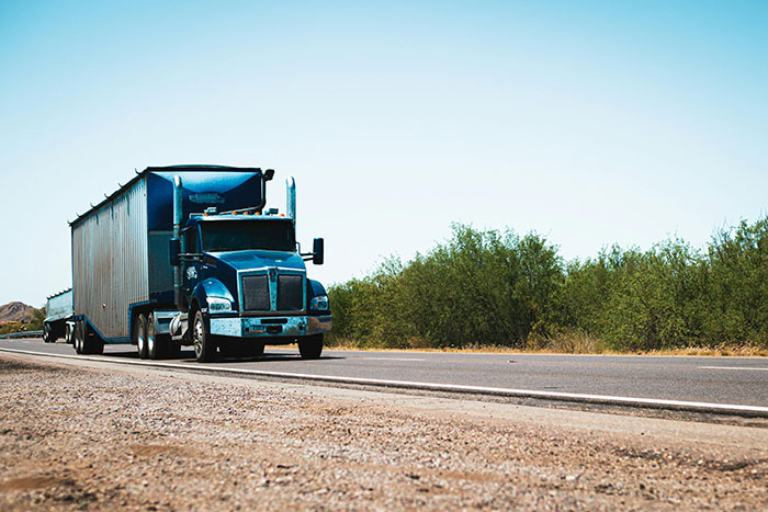 A blue semi-truck drives down a highway on a clear day, highlighting potential for road rage.