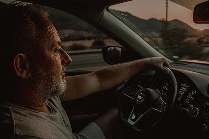 A man driving at sunset, holding the steering wheel, showcasing the drivers on the road and road rage experiences.