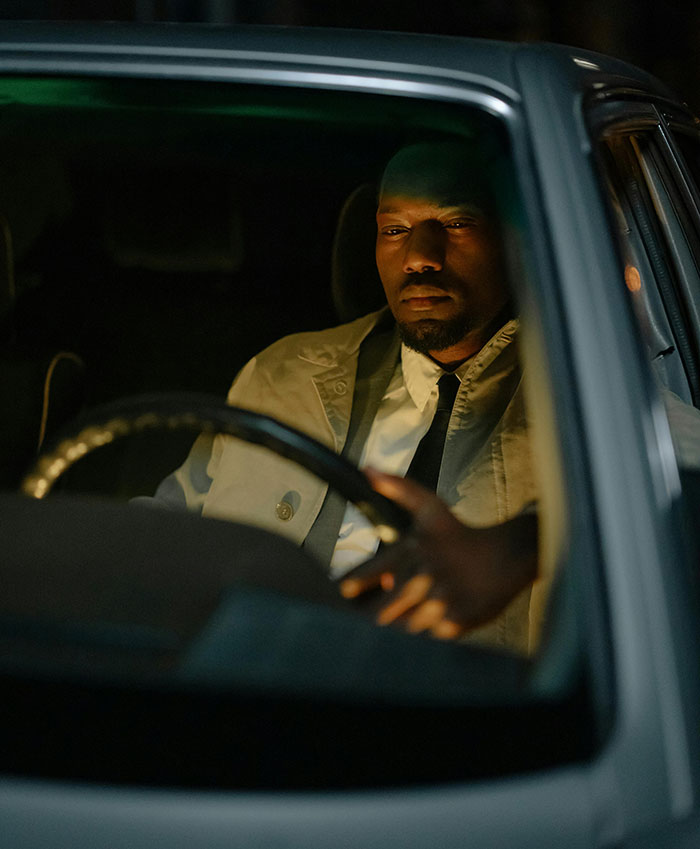 A man with a serious expression gripping a steering wheel, looking forward in a car at night, depicting drivers and road rage.