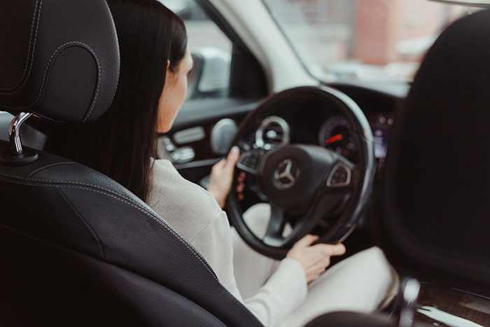 A woman driving a Mercedes, viewed from the back seat, illustrating a calm driver amidst potential road rage scenarios.