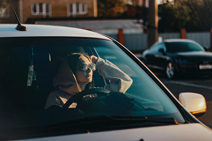 A young driver in sunglasses, looking stressed or anxious, experiencing road rage in traffic.