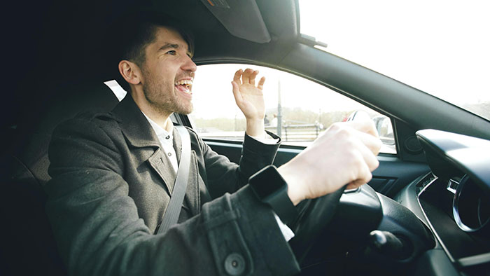 A man in a car, yelling and gesturing with frustration, demonstrating road rage. He's wearing a coat and a seatbelt.