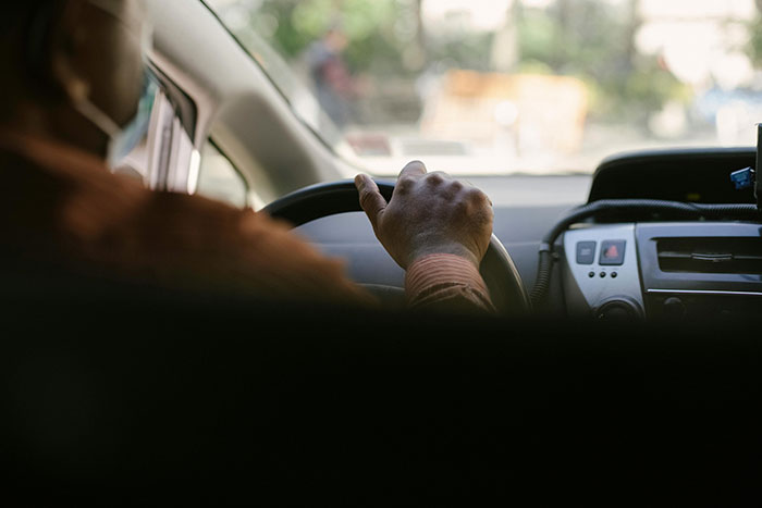 A driver, wearing a face mask, with a hand gripping the steering wheel, indicating road rage or stress.