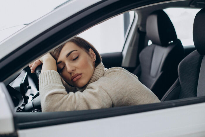 Tired woman sleeping with head on car steering wheel