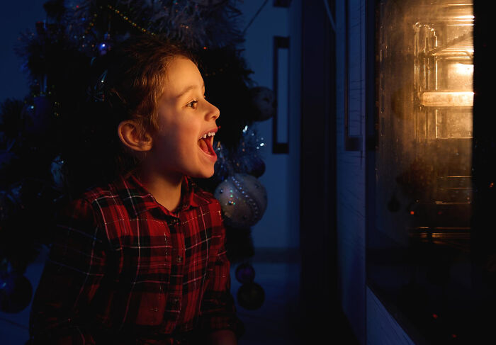 Girl excitedly watching oven glowing through window at night