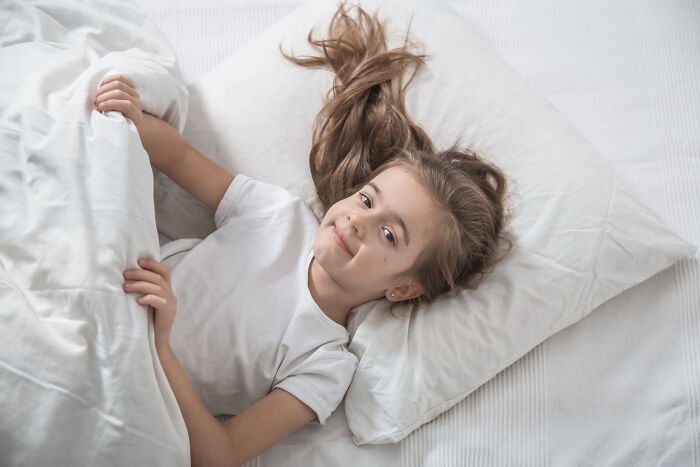 Smiling girl lying in bed under white covers real nightmare starts after waking up