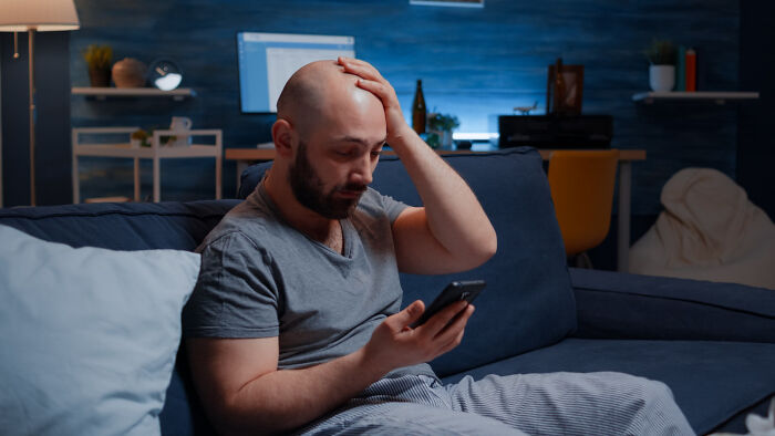 Stressed man holding phone sitting on couch in dark room real nightmare starts after waking up