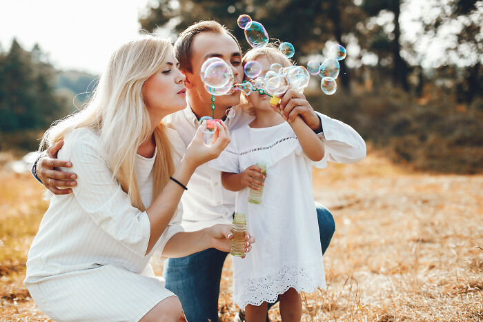 Family blowing bubbles together outdoors in sunny field