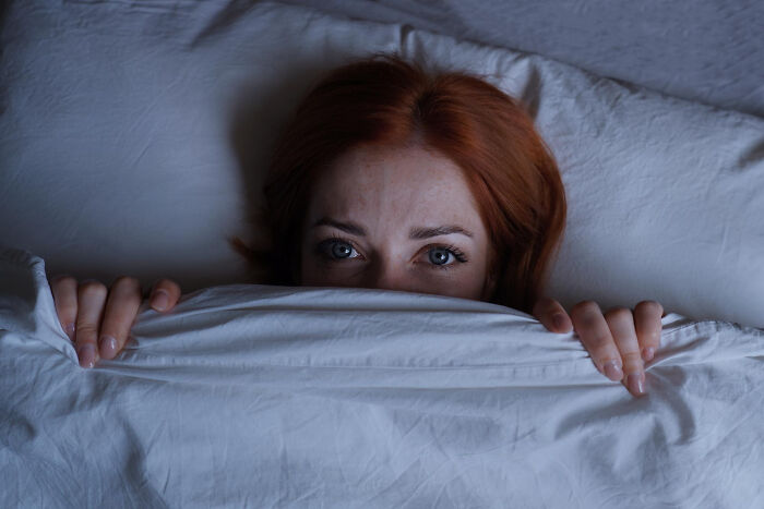Woman hiding under blanket with fearful eyes in bed
