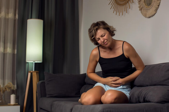 Woman sitting on couch holding stomach in pain after waking up