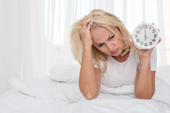 Woman holding clock looking stressed waking up from nightmare