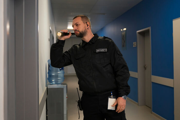 Security guard patrolling hallway with flashlight at night