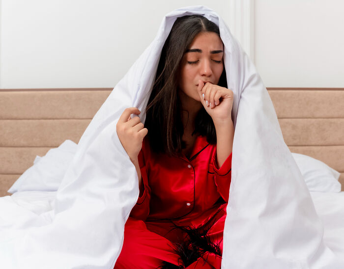 Woman in red pajamas looking distressed under white blanket nightmare
