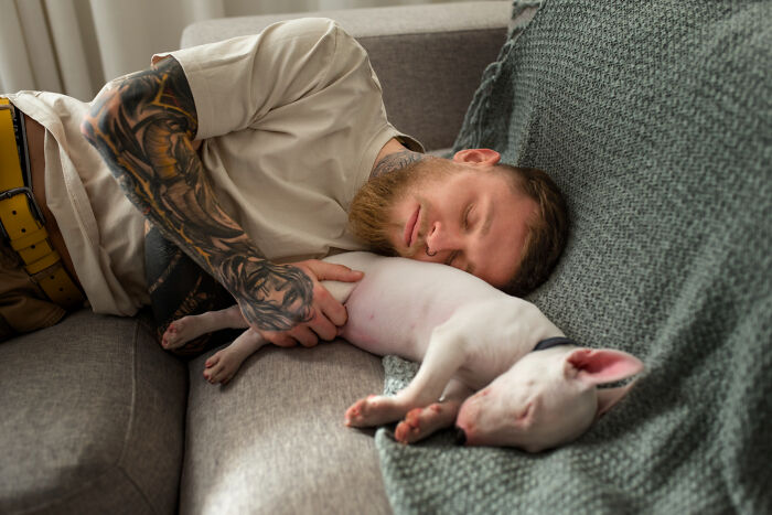 Man with tattoos sleeping on couch holding white dog showing real nightmare peace