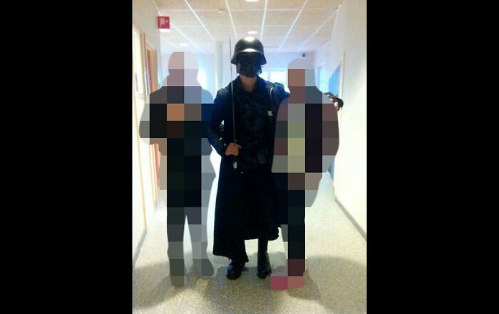Creepy photo of a person in dark costume with helmet standing between two pixelated figures indoors