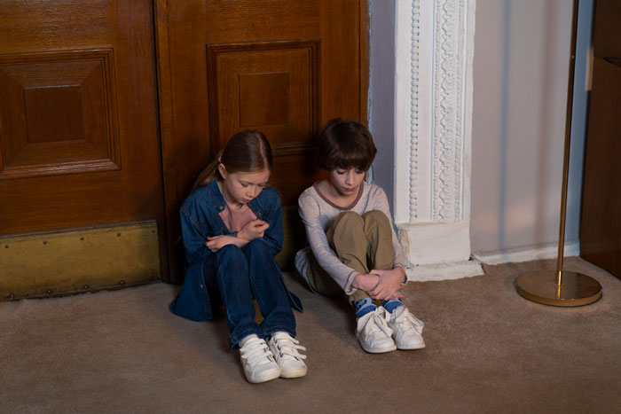 Two sad children sitting on floor near wooden door Two sad children sitting on floor near wooden door