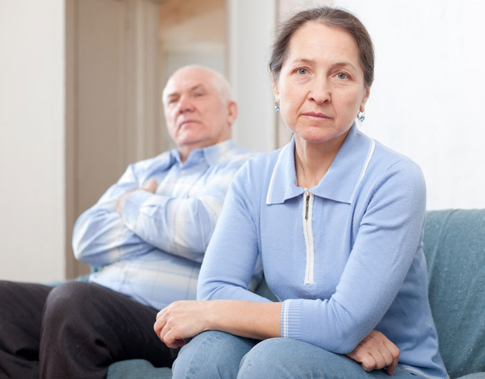 Older couple sitting apart looking serious and distant at home Older couple sitting apart looking serious and distant at home