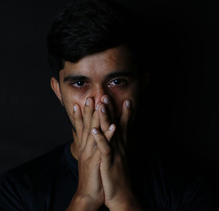Portrait of a young man crying and covering his mouth with his hands Portrait of a young man crying and covering his mouth with his hands