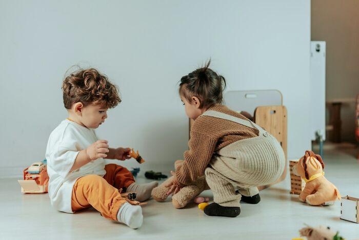 Two toddlers playing on the floor with toys. One child sits, the other crouches, a visual metaphor for the struggles men as a group are suffering.
