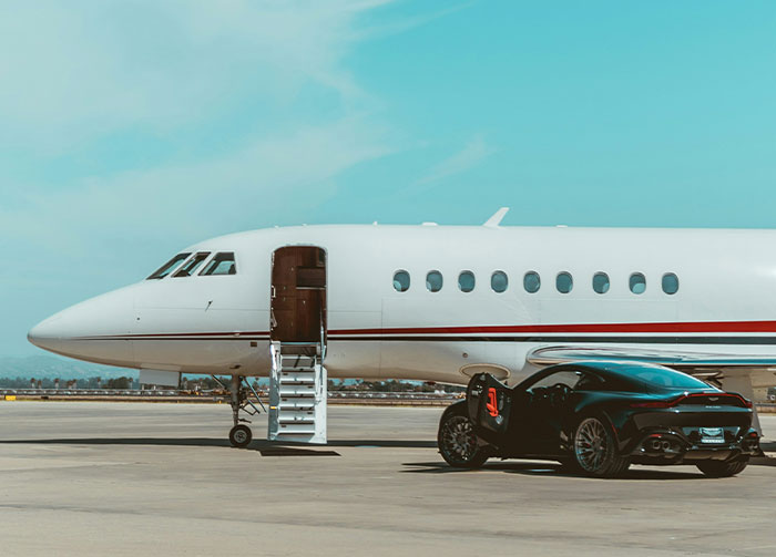 A luxury black sports car parked next to a private jet with its door open, representing controversial beliefs about wealth.