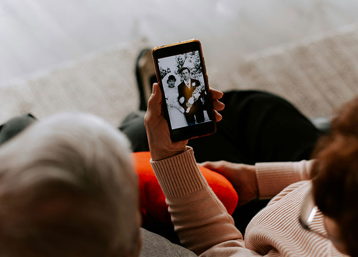 An older person holds a phone displaying a black and white wedding photo, sparking potentially controversial beliefs.
