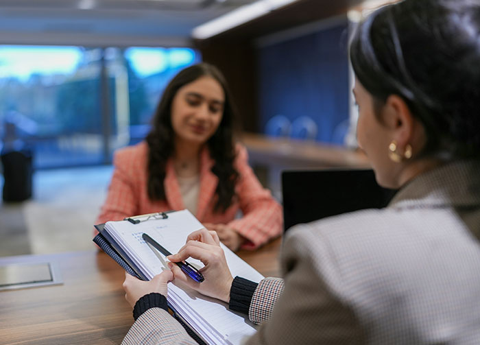 Two women discussing notes. One points to a document while the other listens, representing how controversial beliefs can start arguments.