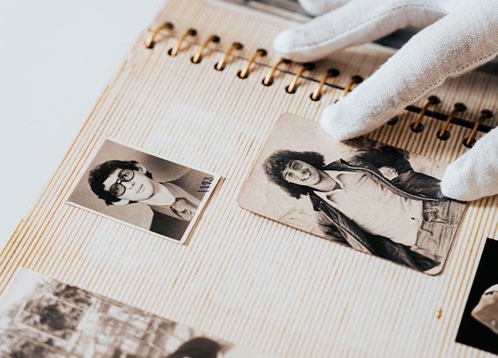 Hands in white gloves carefully hold a black and white photo in an album, showing an old controversial beliefs image.