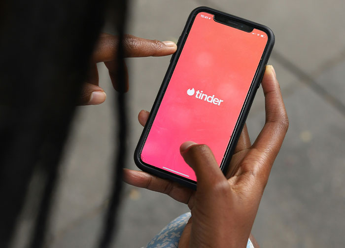 Close-up of a person's hands holding a smartphone displaying the Tinder app. This might instantly start arguments.
