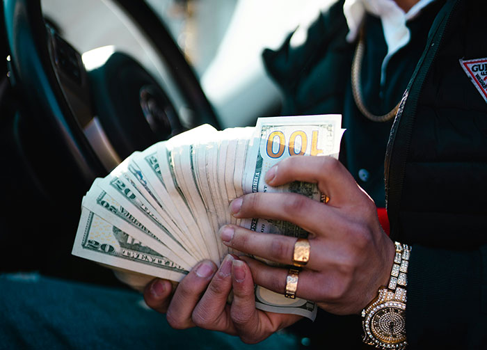 A person holding a large stack of money, including hundred and twenty dollar bills, in a car. This could start arguments.