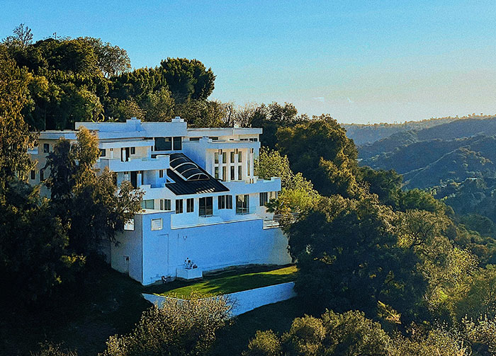 A striking white modern house nestled among lush green hills under a bright blue sky, sparking controversial beliefs.