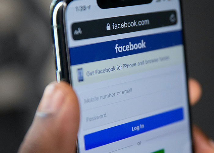 A hand holds an iPhone displaying the Facebook login page, reflecting controversial beliefs about social media.