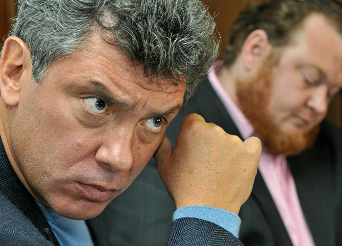 A man with gray, curly hair looks intently, fist to his temple, reflecting on controversial beliefs.