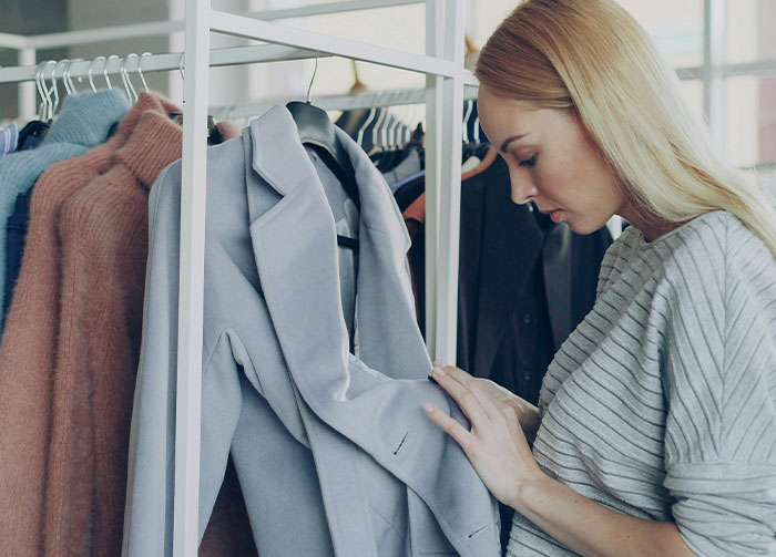 A blonde woman in a grey top examining clothes on a rack, symbolizing choices that might start arguments.