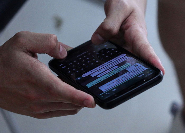Hands holding a smartphone with a messaging app open, showing conversations that might instantly start arguments.