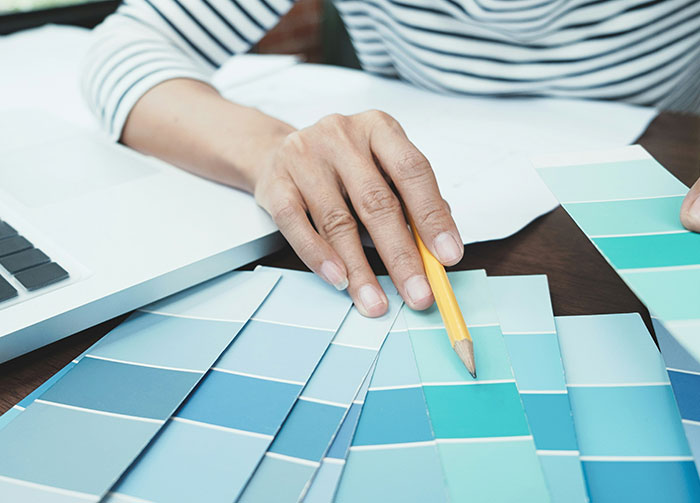 A person in a striped shirt points a pencil at blue color swatches, considering controversial beliefs that might start arguments.