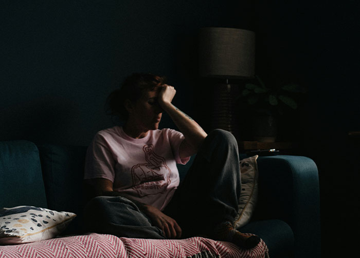 A woman sits on a couch, hand on her forehead, looking stressed. This image could spark controversial beliefs.