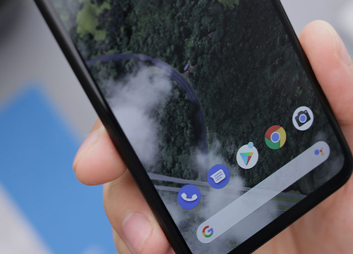 A hand holds a smartphone with a green forest wallpaper. Several app icons are visible. Might instantly start arguments.