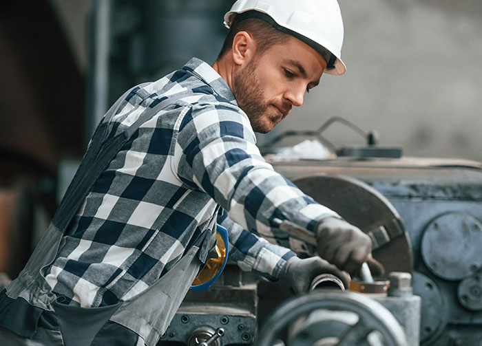 Man in a hard hat and plaid shirt working on machinery, sparking arguments about controversial beliefs.