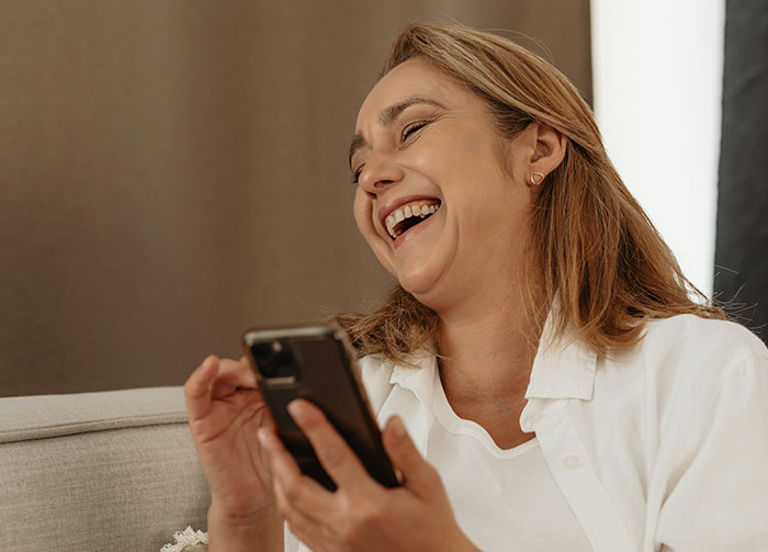 A woman laughing heartily while looking at her phone. This image relates to controversial beliefs that might start arguments.