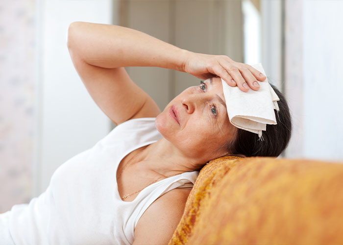 Postmenopausal woman experiencing hot flashes and brain-sapper symptoms sitting on couch Postmenopausal woman experiencing hot flashes and brain-sapper symptoms sitting on couch