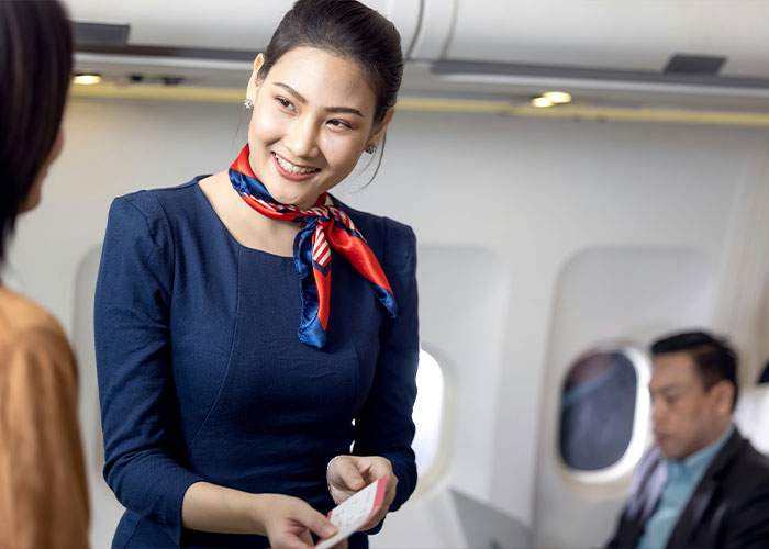 Flight attendant smiling, checking passenger boarding pass on plane
