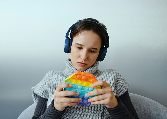A young woman with headphones looking at a pop-it toy, representing new research on autism and understanding the condition. A young woman with headphones looking at a pop-it toy, representing new research on autism and understanding the condition.